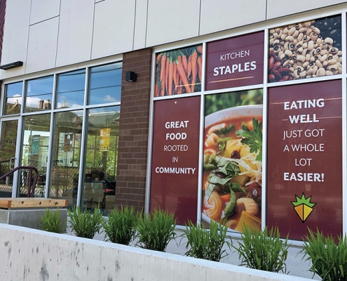Exterior view of Gem City Market, Dayton OH. Facade is made up primarily of large floor-to-ceiling windows which are filled with bright, simple food photos and branded messaging in each panel